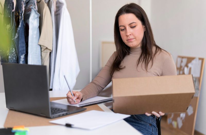 Woman working with a laptop and a box in a home office.